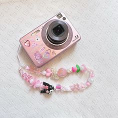 a pink camera sitting on top of a table next to a beaded lanyard