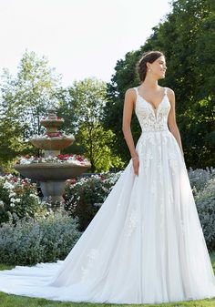 a woman in a white wedding dress standing on the grass near some bushes and flowers