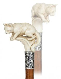 two white cats sitting on top of an ornate vase with a wood base and wooden handle