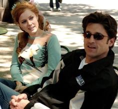 two people sitting next to each other on a bench in the park, one person wearing sunglasses