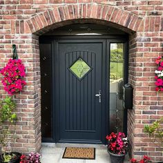 a black front door surrounded by flowers and potted plants on the side of a brick building