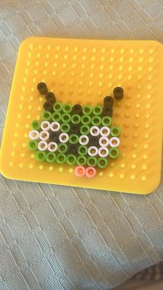 a close up of a beaded animal on a yellow tray with a person's feet in the background