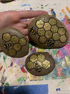 two painted rocks with bees on them, one being held by a person's hand