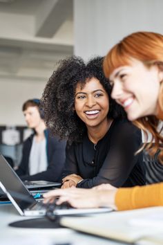 two women sitting at a table with laptops in front of them, both smiling