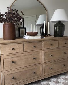 a dresser with a mirror, lamp and vase on it in a living room area