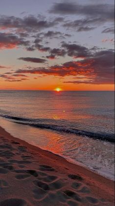 the sun is setting over the ocean with footprints in the sand