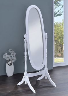 a white vanity mirror sitting on top of a wooden floor next to a vase with flowers