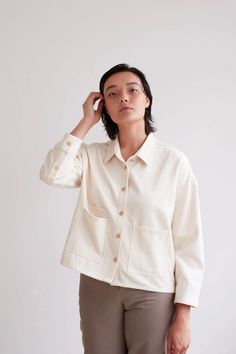 a woman in a white shirt and khaki pants is holding her hand up to her ear