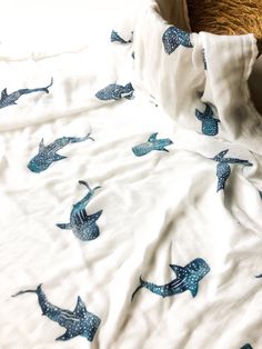 an unmade bed with white sheets and blue whale designs on the comforter, next to a brown teddy bear