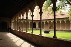 an outdoor courtyard with arches and stone flooring, surrounded by green grass and trees