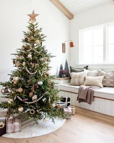 a decorated christmas tree in the corner of a room with white walls and wood floors