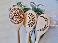 three wooden spoons with designs on them sitting in front of a white flower arrangement