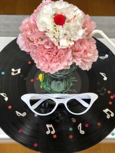 a vase filled with pink flowers and white sunglasses on top of a black record covered in confetti