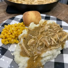 a plate with mashed potatoes, meat and gravy on it next to corn