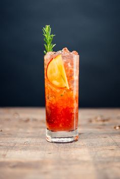 a glass filled with liquid and garnish on top of a wooden table