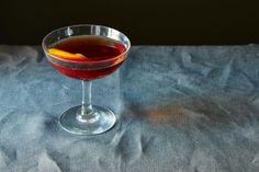 a glass filled with liquid sitting on top of a blue table cloth next to an orange peel