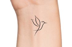 a small black bird tattoo on the right side of the arm, with an outline of a flying bird