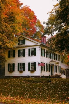 a large white house with green shutters and trees in the front yard on an autumn day