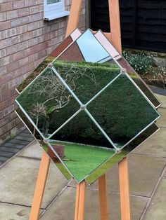 a mirror sitting on top of a wooden easel next to a brick wall and grass