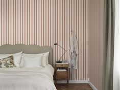 a white bed sitting next to a window in a room with striped wall paper on the walls