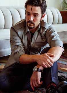 a man sitting on the floor in front of a couch with his hand on his knee