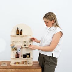 a woman standing in front of a wooden shelf with bottles and other items on it