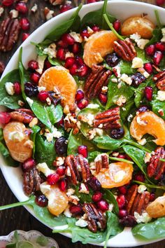 a white bowl filled with spinach salad topped with oranges and pecans