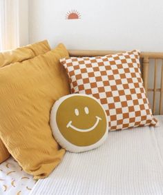 a smiley face pillow sitting on top of a bed next to two orange and white pillows