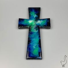 a glass cross that is sitting on a table next to a white wall with a blue and green painting on it