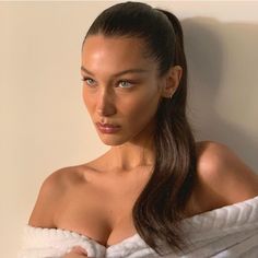 a woman with long hair wrapped in a towel looking at the camera while standing against a wall