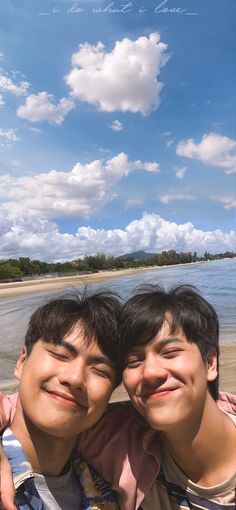 two young men standing next to each other on a beach under a blue cloudy sky