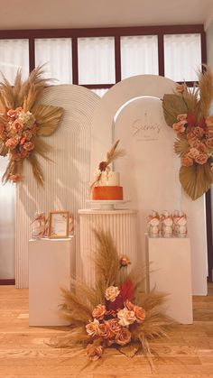 an arrangement of cakes and flowers on display in front of a white wall with wooden flooring