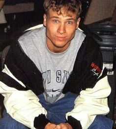 a young man sitting in a chair with his hands on his knees and looking at the camera