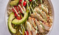 a white bowl filled with chicken, rice and avocado garnished with dressing