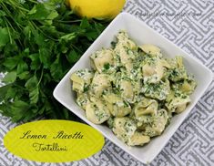 a white bowl filled with pasta next to lemon and parsley