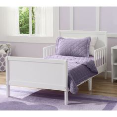 a white toddler bed with purple bedspread