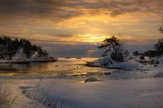 the sun is setting over an icy lake with trees and snow on the ground in front of it