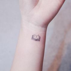 a small tattoo on the wrist of a girl reading a book with an open bookmark