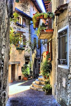 an alley way with stone buildings and plants growing on the balconies