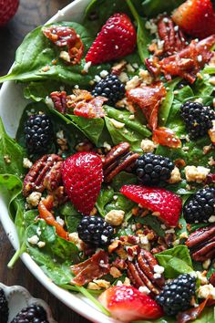 spinach salad with berries, pecans and nuts in a white bowl