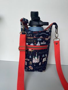 a blue bag with red straps and a black bottle in the back that has buildings on it