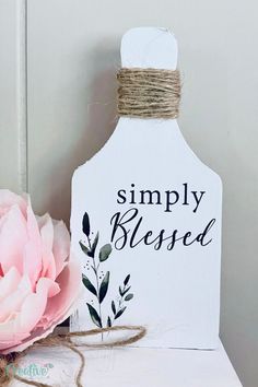 a white wooden sign sitting on top of a table next to a pink flower