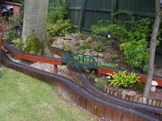 a model train set is shown in the yard with trees and rocks on it's sides