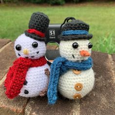 two crocheted snowmen sitting next to each other on top of a rock