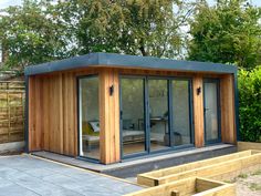 a small wooden building with sliding glass doors on the front and side windows, in a garden area