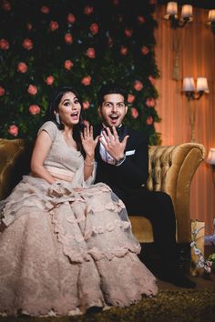 a man and woman sitting on a couch in front of a flower covered wall with roses