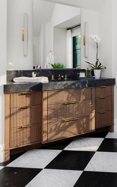 a black and white checkered floor in a bathroom with two sinks, mirrors and plants