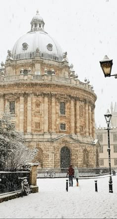 two people standing in front of a building on a snowy day with snow falling all around