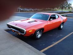 an orange muscle car parked in a parking lot next to a curb with no one around it