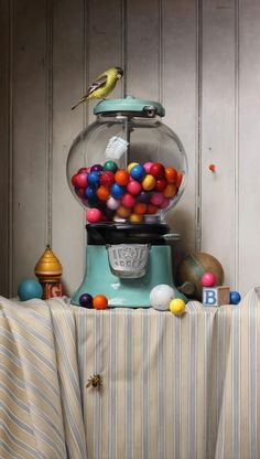 a painting of a gumball machine with a bird on it's top and balls in the bottom